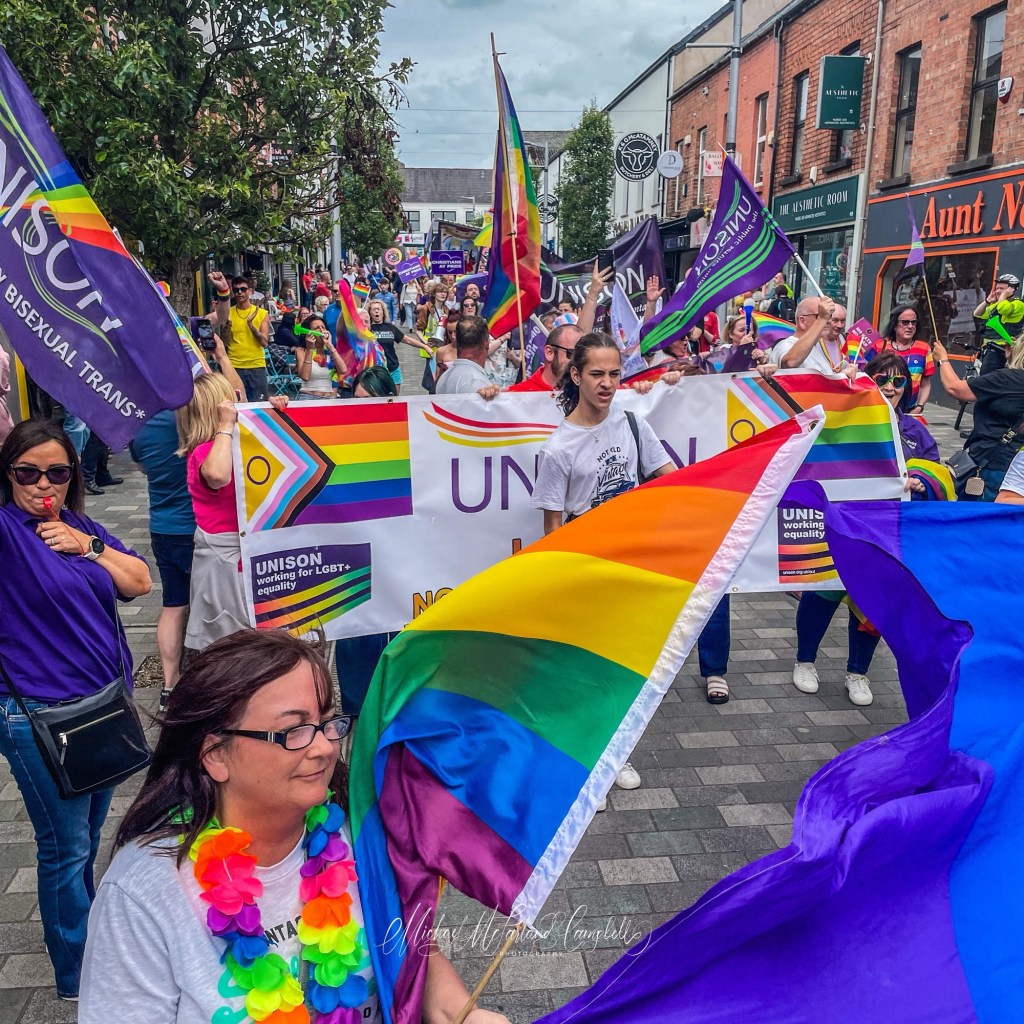 Pride parade participants carrying rainbow flags and banners through Ballymena town centre