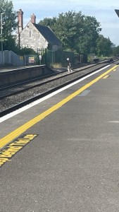 Person walking across railway tracks between platforms at Mainistir Eimhín station.